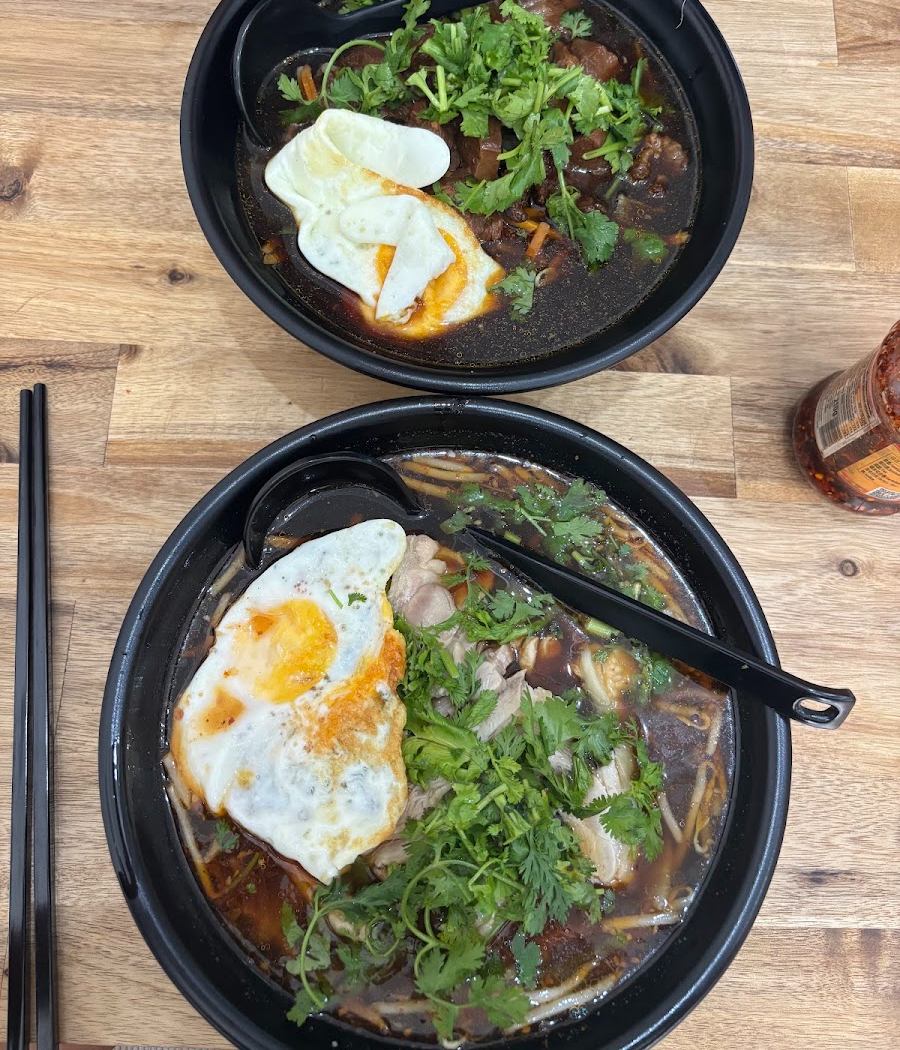 Deux soupes de nouilles garnies de coriandre et d'un œuf au plat, dans des bols noirs sur une table en bois